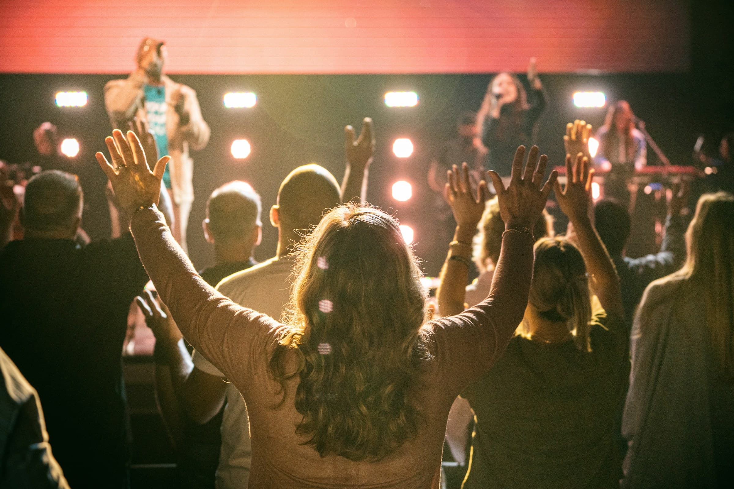 A congregation lifting their hands in worship in warm evening light